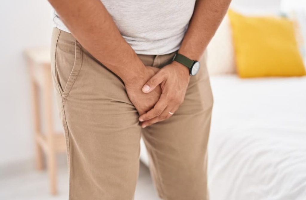 homem de calça com as duas mãos sobre o pênis