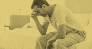 Homem com semblante preocupado, sentado na cama com a mão na cabeça