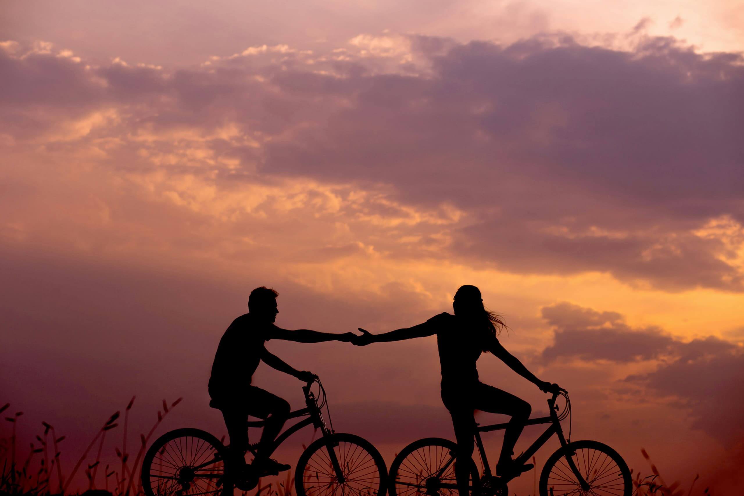pareja de manos dadas en bicicleta al atardecer