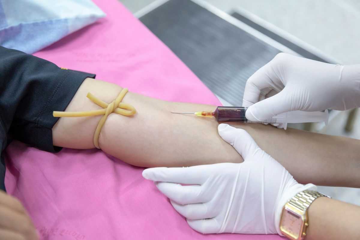 Healthcare professional inserting a needle into a man's arm to draw blood.