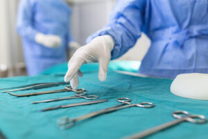 Cirurgia da doença de Peyronie: Equipamentos médicos sob uma mesa coberta com tecido azul. Na lateral esquerda, um profissional da área da saúde veste uma vestimenta azul e luvas brancas.