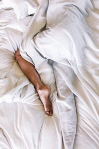 Imagem mostra uma pessoa na cama deixada embaixo de lençóis brancos e simboliza como ajudar marido com disfunção erétil.