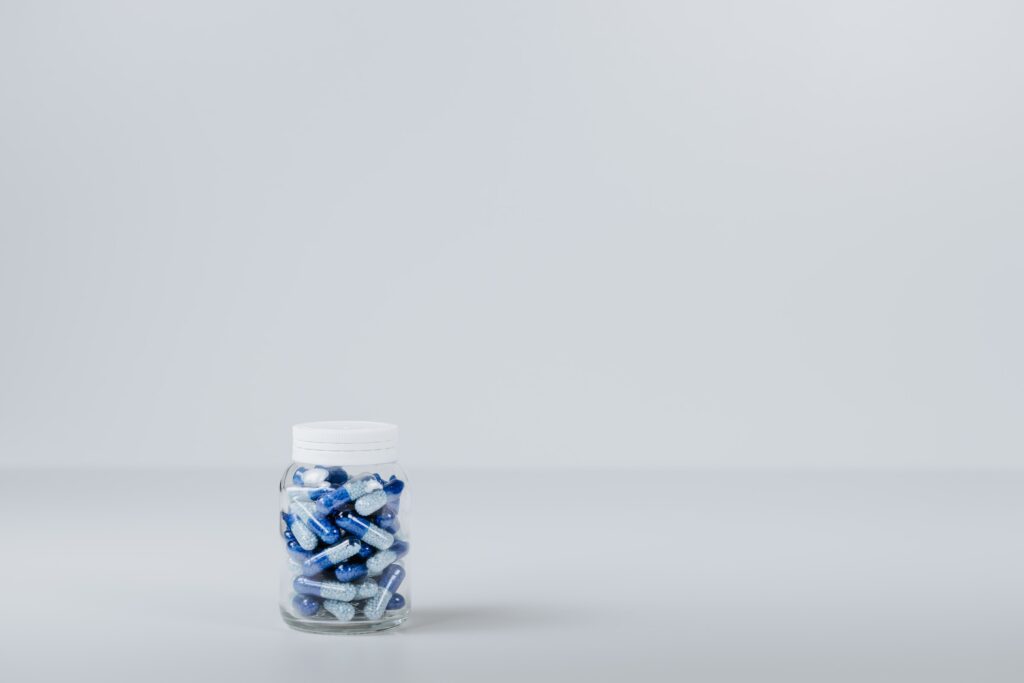Fundo e superfície brancas com recipiente com pílulas azuis simulando Tadalafila e Sildenafila para Pacientes com Doenças Cardiovasculares