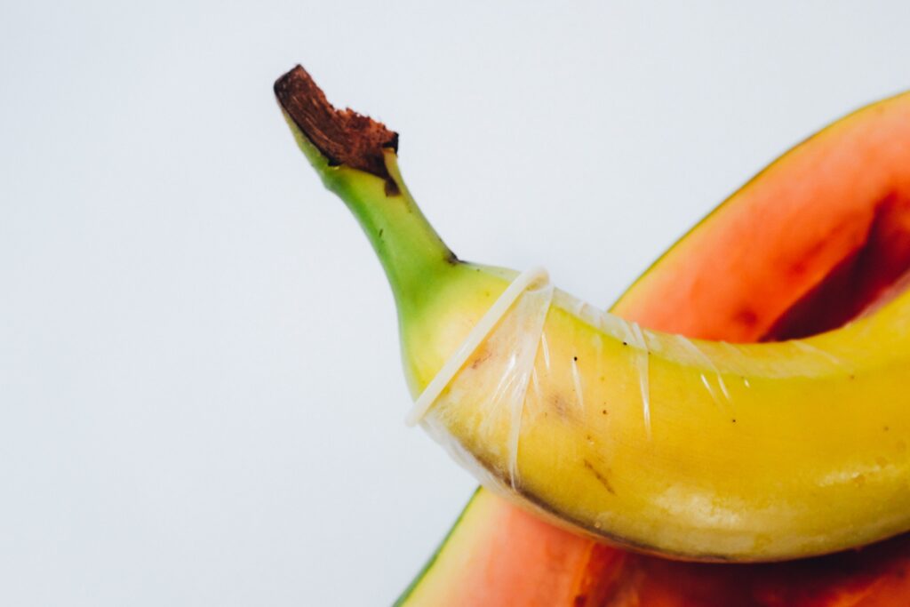 Superfície branca com uma banana com camisinha e um pedaço de mamãe simbolizando a perda de sensibilidade no pênis no sexo