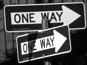 Duas placas de trânsito preta com seta branca e mensagem "one way" indicando para a direita. Elas representam a ejaculação anterógrada.