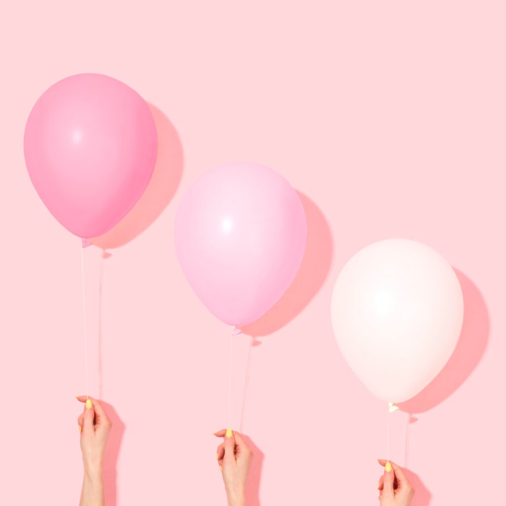 Fundo rosa com três mãos segurando balões cor de rosa de tamanhos e alturas diferentes representando as alternativas para o uso do extensor peniano