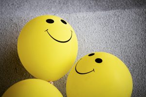 Fundo branco texturizado e balões amarelos com rostos felizes simbolizando os efeitos colaterais de antidepressivos para a saúde sexual