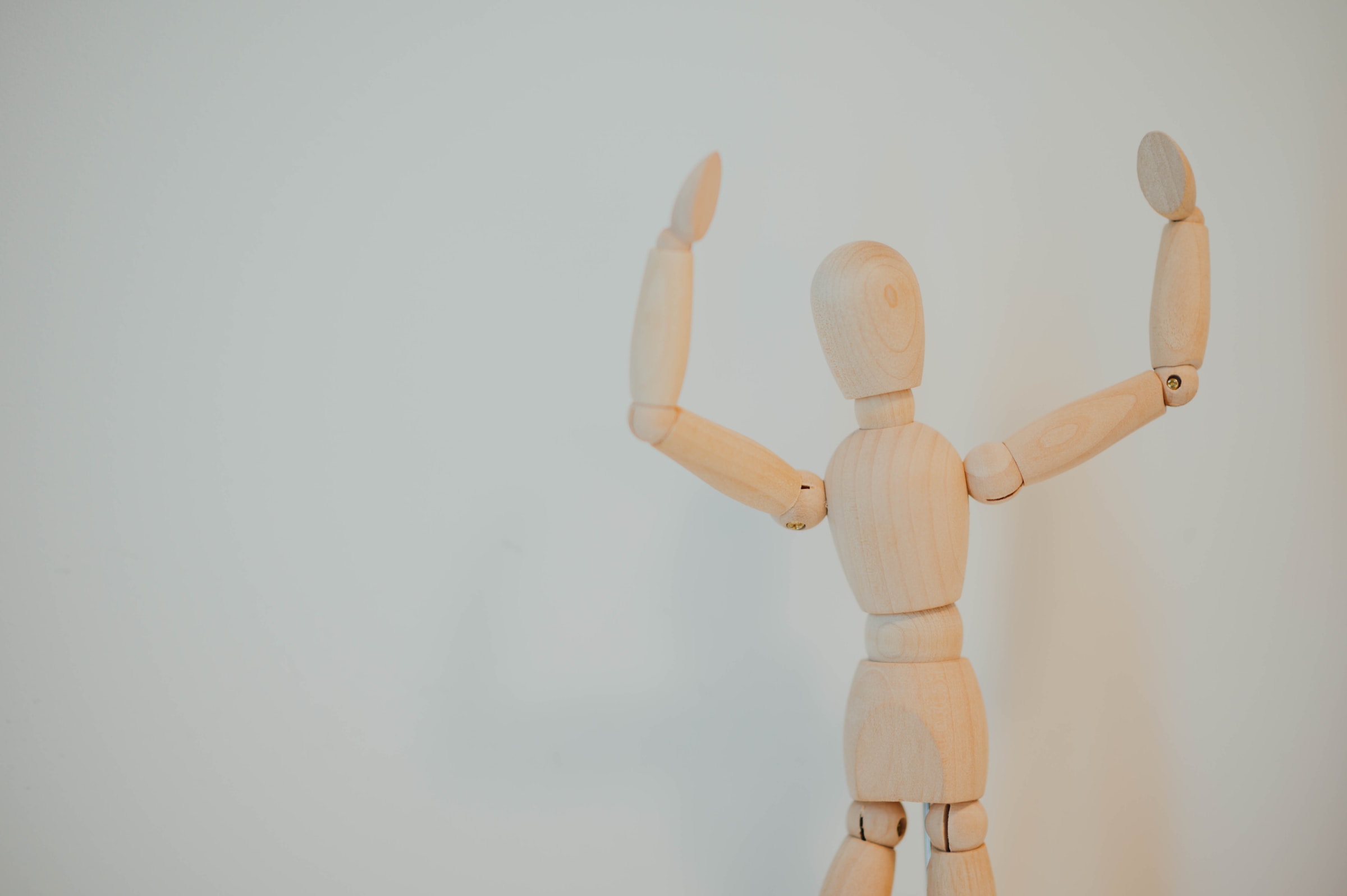 Fundo branco e boneco de madeira clara em primeiro plano com gesto que indica algo grande e simboliza o extensor para prótese peniana