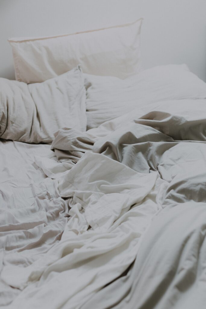 Cama com lençóis e travasseiros brancos bagunçados representando os efeitos do sono para a saúde sexual masculina