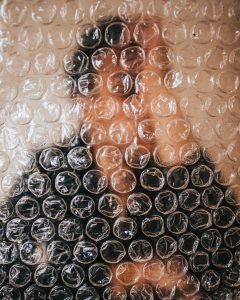 Plástico bolha transparente em primeiro plano e homem com camisa de cor escura e mão na cabeça desfocado em segundo plano simbolizando a preocupação com tipos de verrugas no pênis