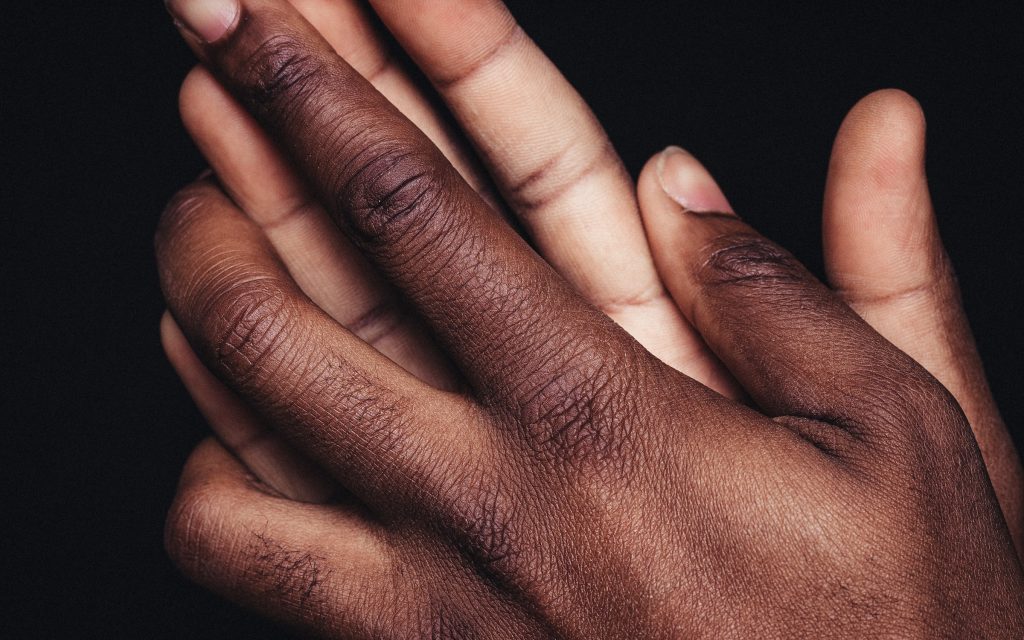 Fundo preto e mãos de homem negro se tocando em close representando os exames para diagnóstico de fibrose peniana
