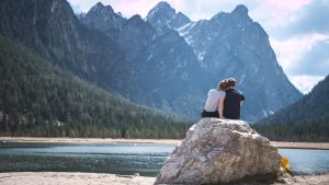 Paisagem romântica com montanhas e lago ao fundo e um casal sobre uma pedra à direita em primeiro plano representando a Doença de Peyronie e sexualidade