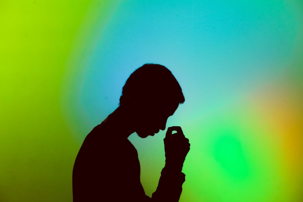 Fundo colorido em verde, azul e laranja com silhueta de homem cabisbaixo com a mão na ponta do nariz preocupado com a disfunção erétil psicogênica