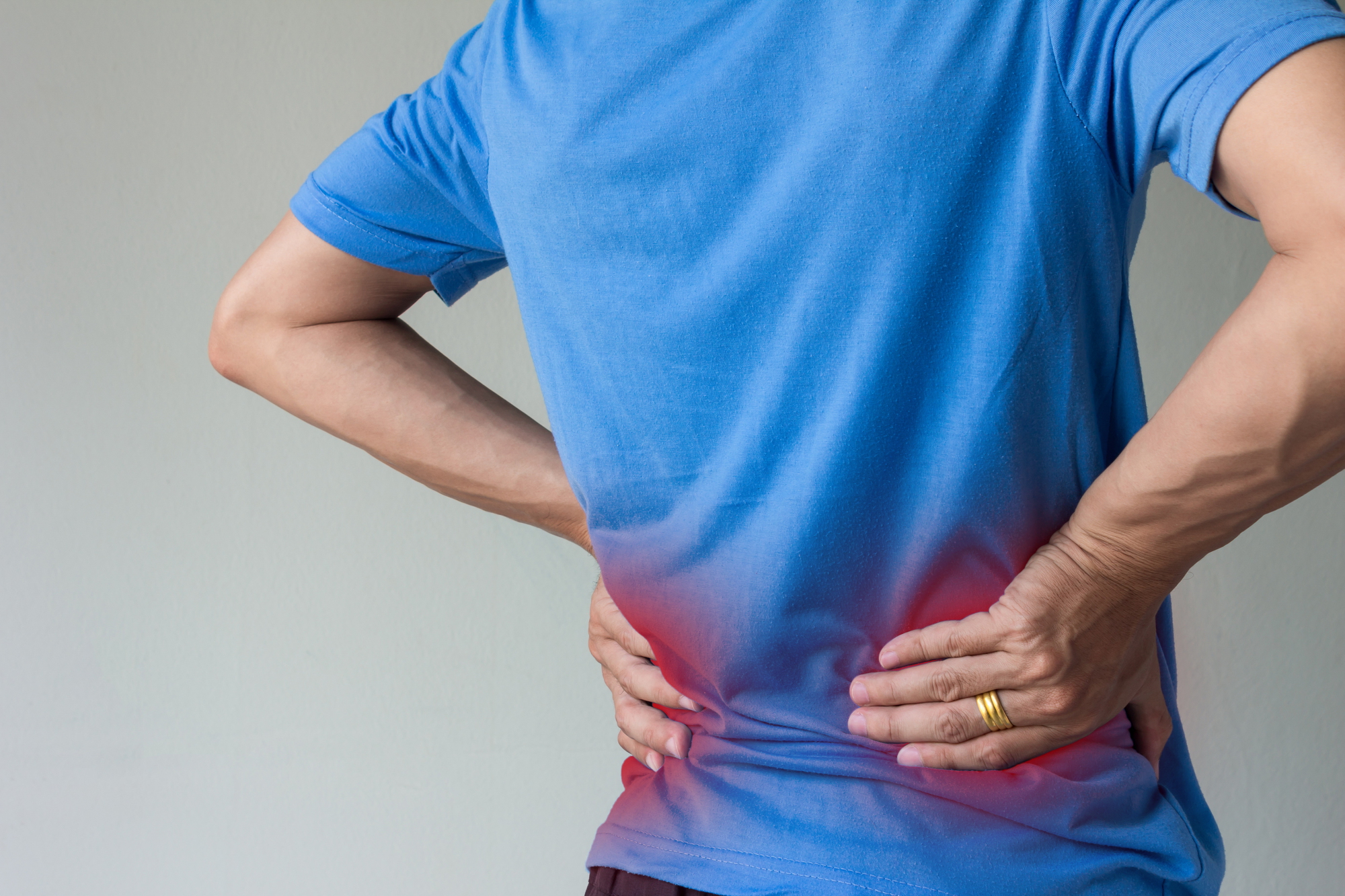 Homem com má postura segura a região lombar, destacada em vermelho para indicar dor e representa um dos maus hábitos que afetam a saúde sexual do homem