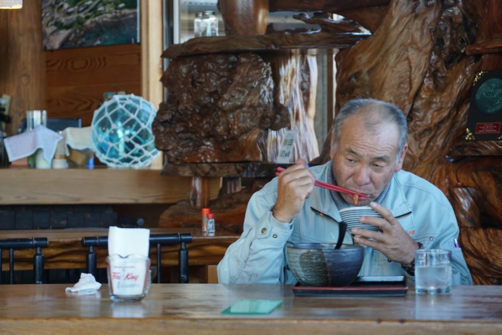 Elderly Asian man on the left in a restaurant eating with a bowl and chopsticks representing foods that naturally boost testosterone