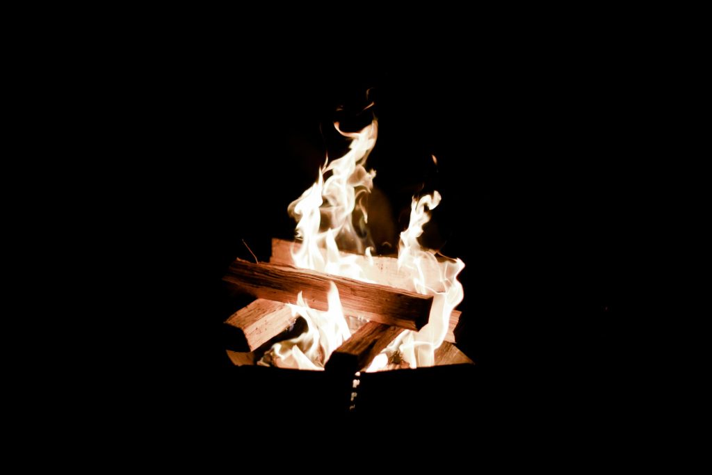 Fundo preto com fogueira feita sobre alguns blocos de madeira simbolizando pênis ardendo