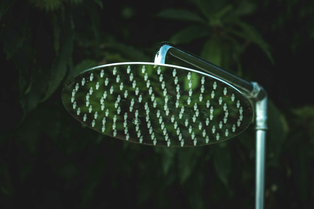 Dark background with the top part of a silver shower without water in the foreground representing how to wash the penis