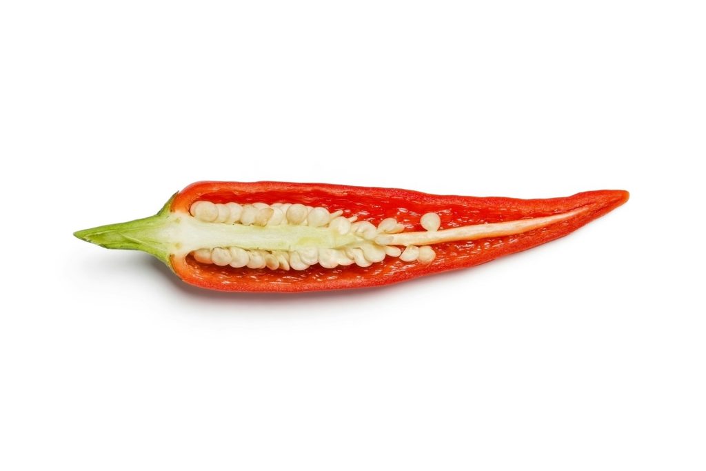 White background with a horizontally cut green-tailed red pepper, exposing the white and small seeds symbolizing low male libido
