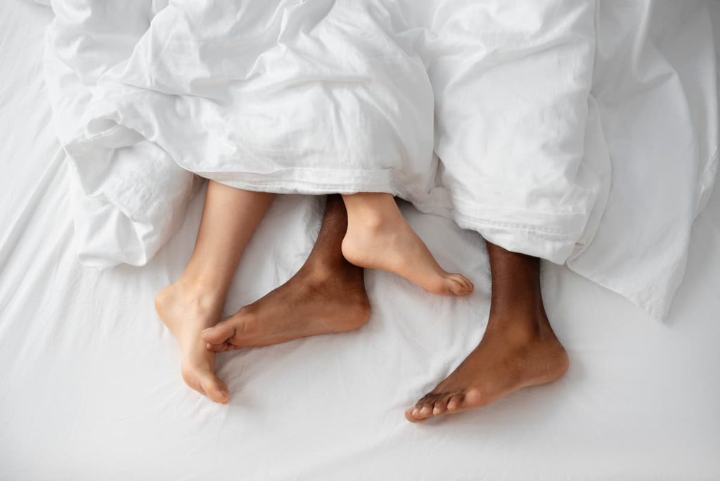 image showing the feet of a couple lying in bed covered by a white sheet