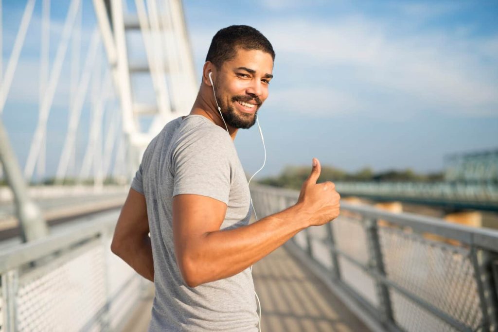 Homem jovem ao ar livre fazendo sinal de positivo com a mão.
