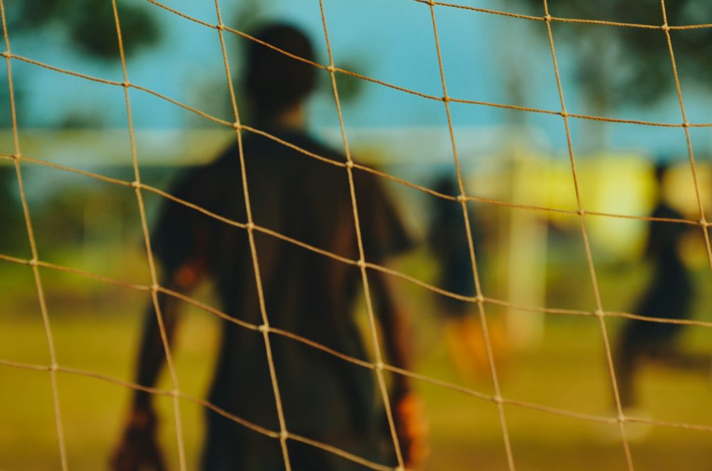 Blurred background with a football team, with a player closer to the goal seen through the net representing penile prosthesis and football