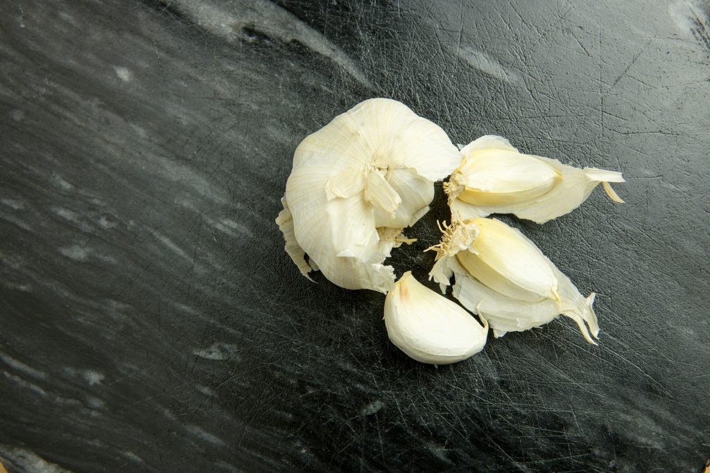 Superfícis cinza com aspecto de pedra com cabeça de alho branca parcialmente despedaçada representando um dos alimentos bons para próstata 