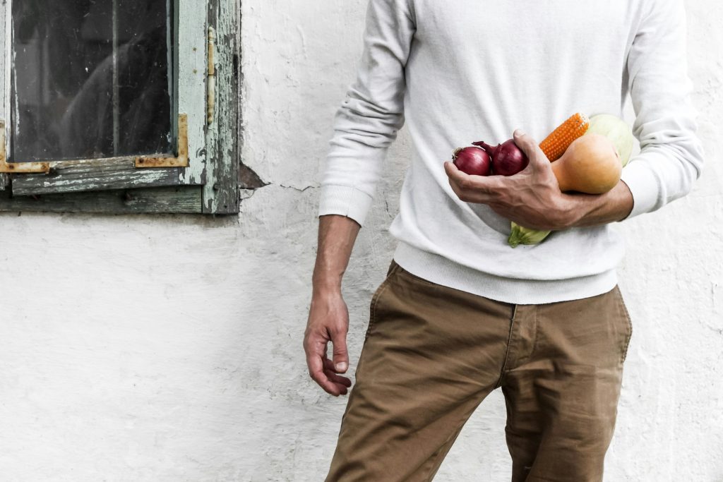 hombre sosteniendo cebollas, zanahoria y calabacín en su mano izquierda