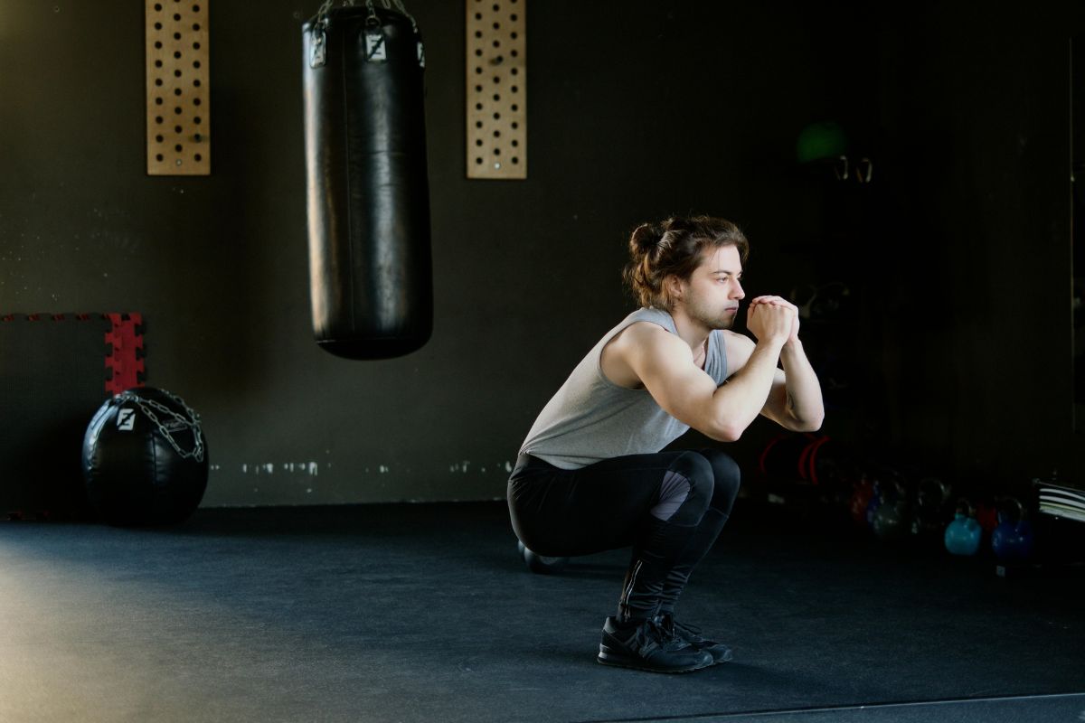 man performing squats in gym next to punching bag