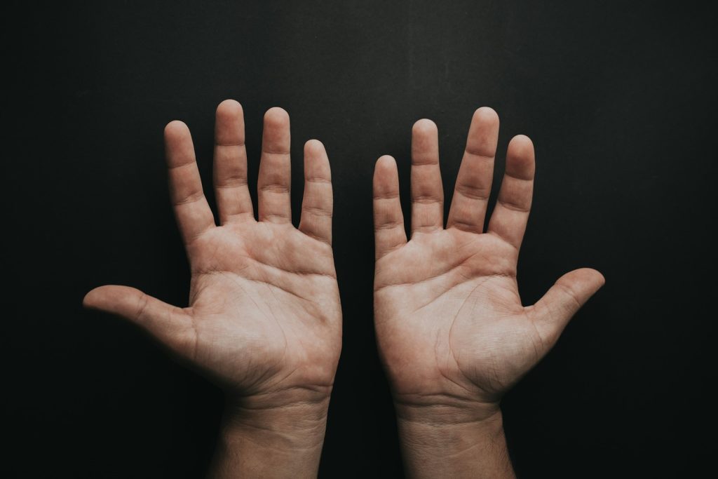 Fundo preto e mãos de homem branco levemente separadas com dedos levemente separados com as palmas viradas para frente simbolizando a masturbação compulsiva
