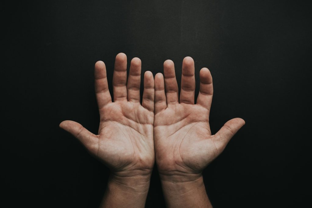 Black background and hands of a white man side by side with fingers slightly separated with palms facing forward symbolizing compulsive masturbation