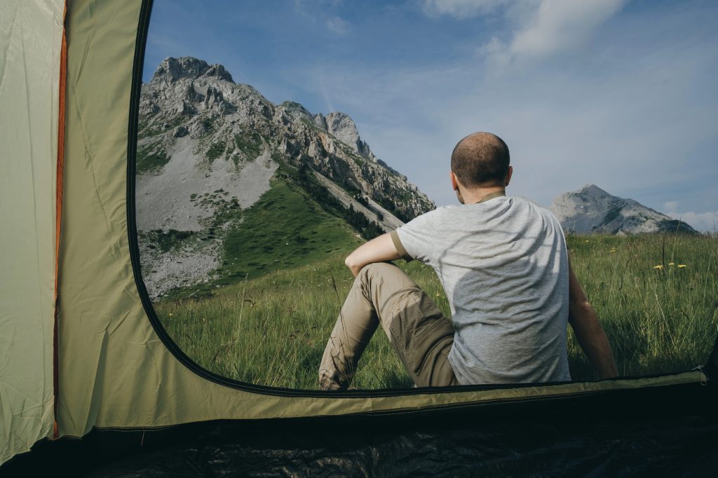 Fundo de montanha e grama, com homem sentado de costas em primeira plano e parte de uma barraca à esquerda representando os remedio natural para impotencia masculina