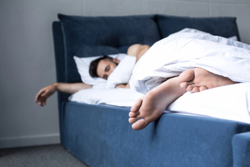 Man sleeping on a bed with headboard and foot out