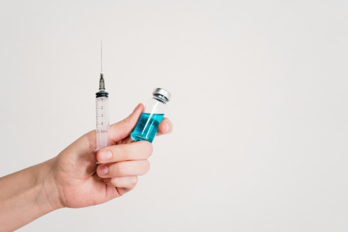 hand holding a syringe and a vial with blue liquid
