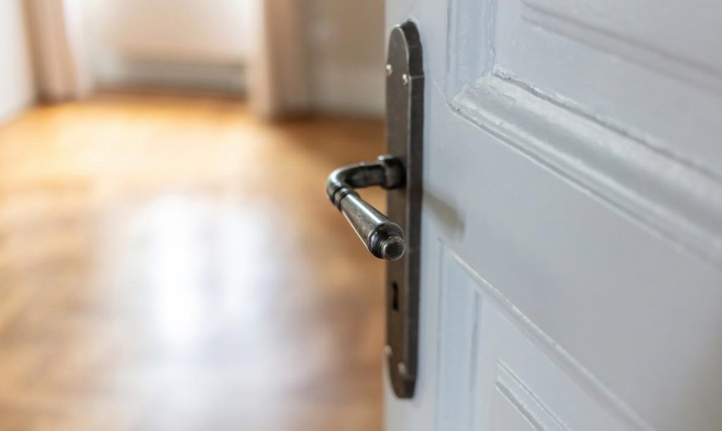 White wooden door with a brown lock open, revealing a room with brown wooden floor and beige walls representing treatment for excess foreskin
