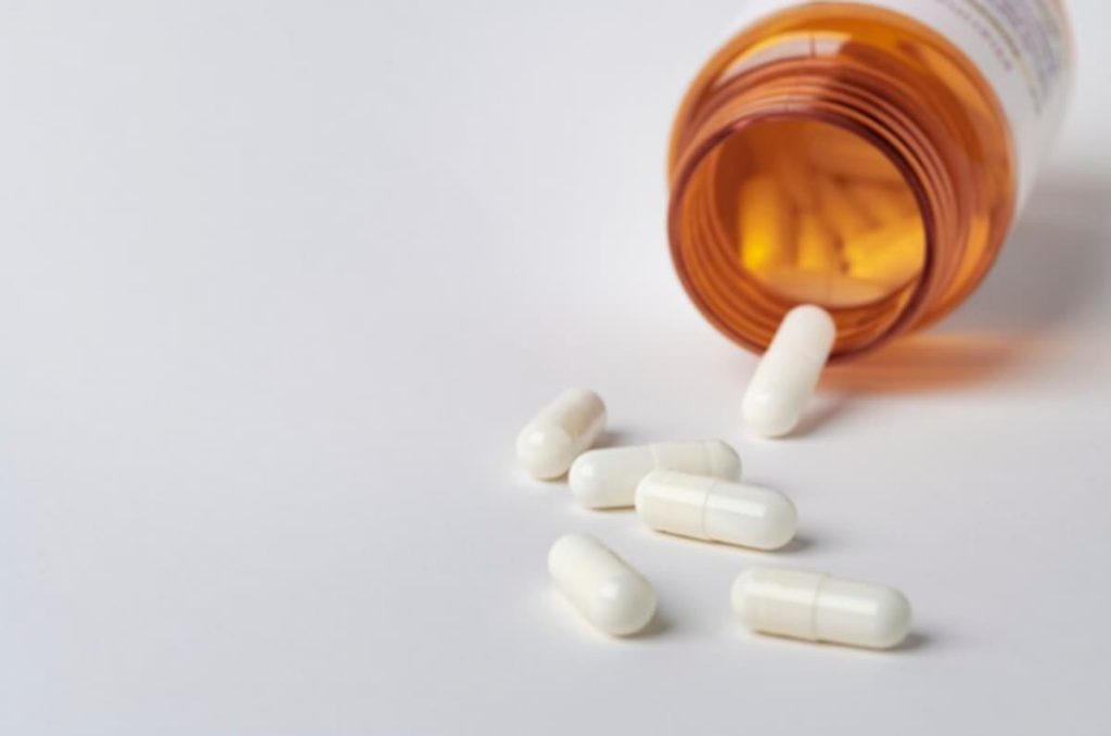 orange medicine packaging lying open with six capsules coming out of it.