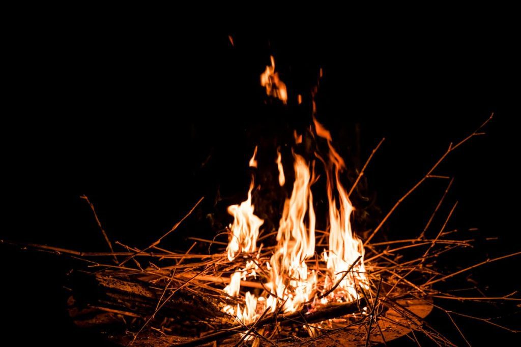 Black background with orange bonfire made with twigs on brown ground