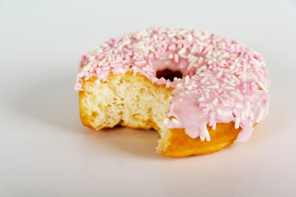 White surface with a bitten donut with pink frosting symbolizing anal sex