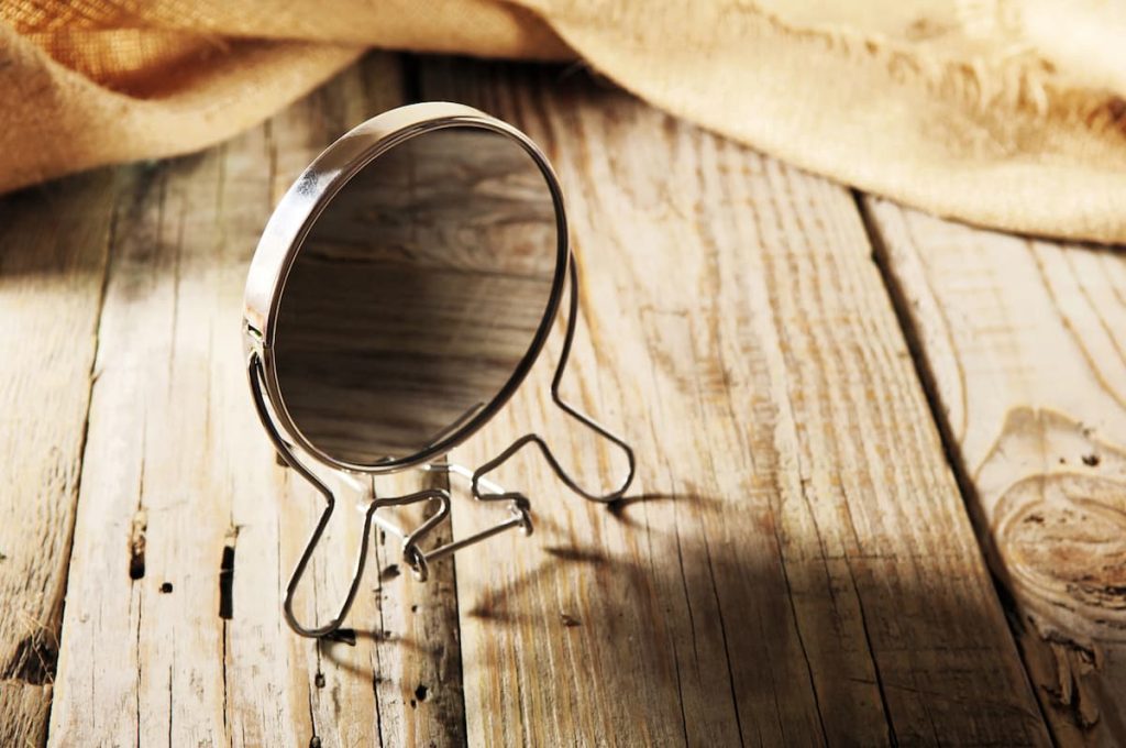 Superfície de madeira clara com espelho de metal prateado posicionado sobre ela representando o autoexame testicular que deve ser feito em frente a um espelho