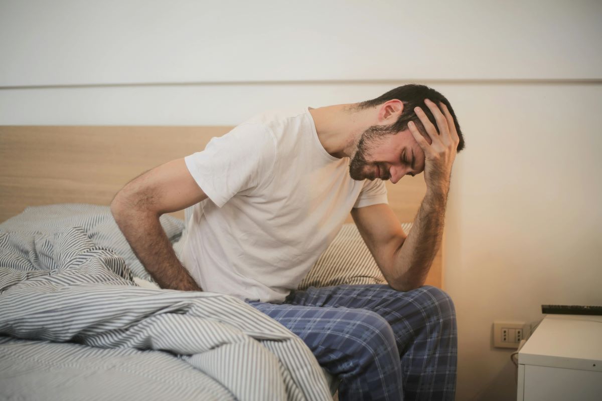 man sitting on the edge of the bed with one hand on his head and looking tired