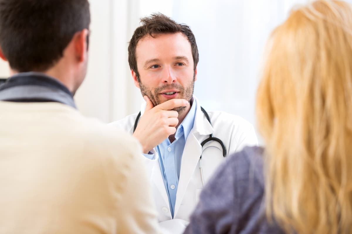 Casal de homem e mulher de costas conversando com médico de frente com estetoscópio no pescoço em consultório médico sobre Quando o homem perde o desejo pela esposa