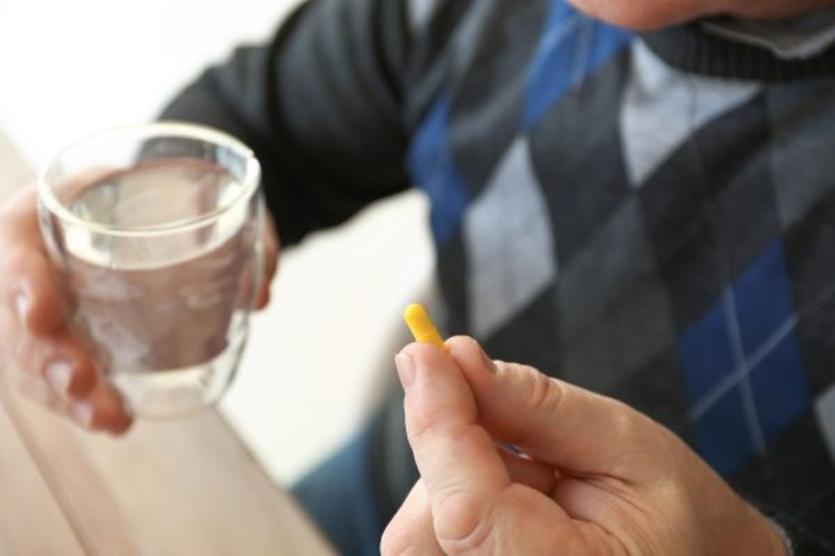 man holding a glass of water in one hand and a capsule in the other hand.