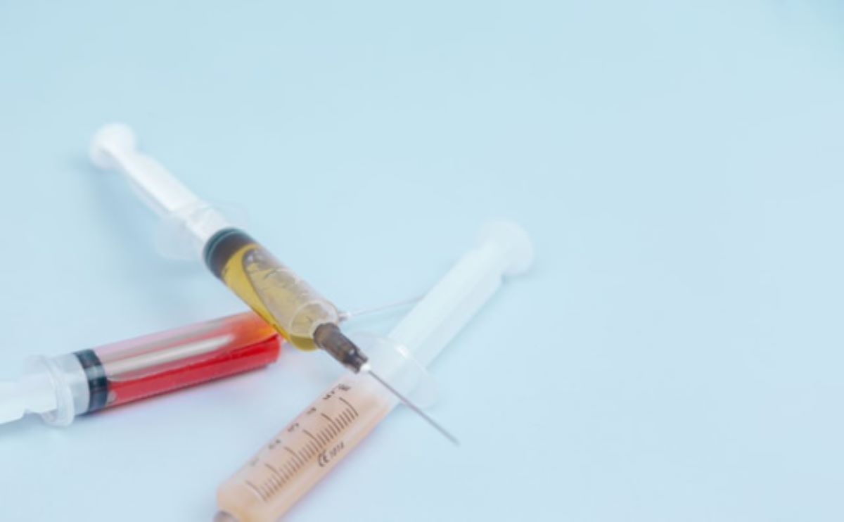 three syringes with yellow, red, and pinkish liquids on a light blue surface