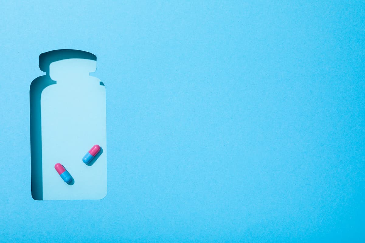 Fundo azul com recorte vazado em formato de frasco de remédio e duas cápsulas simbolizando ioimbina para que serve
