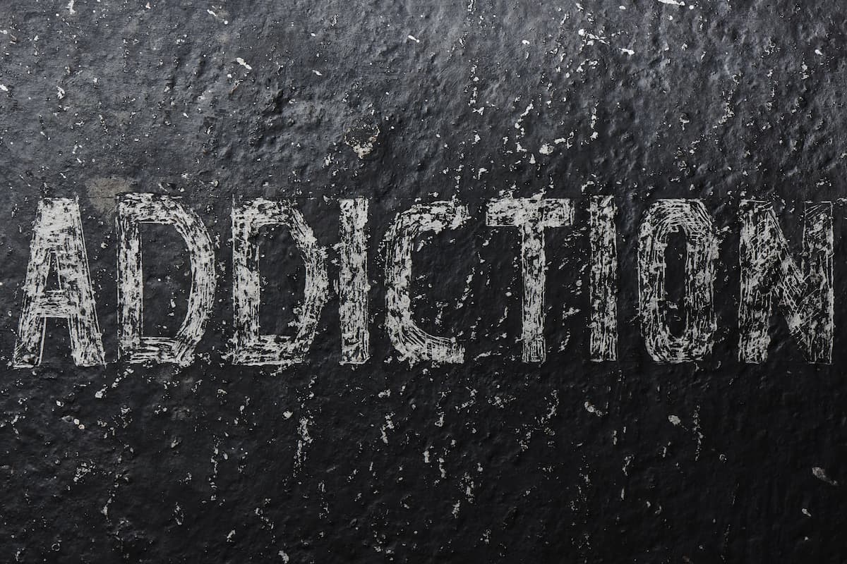 Palavra "ADDICTION" (vício, em inglês) escrita em um estilo desgastado, com letras brancas e texturizadas sobre superfície de pedra ou concreto, representando o vício em sexo