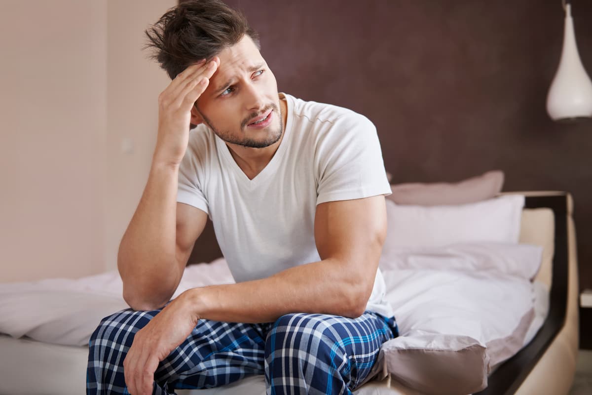 Man sitting on a bed with a worried expression, illustrating reflection or concern about what ejaculation is and possible issues