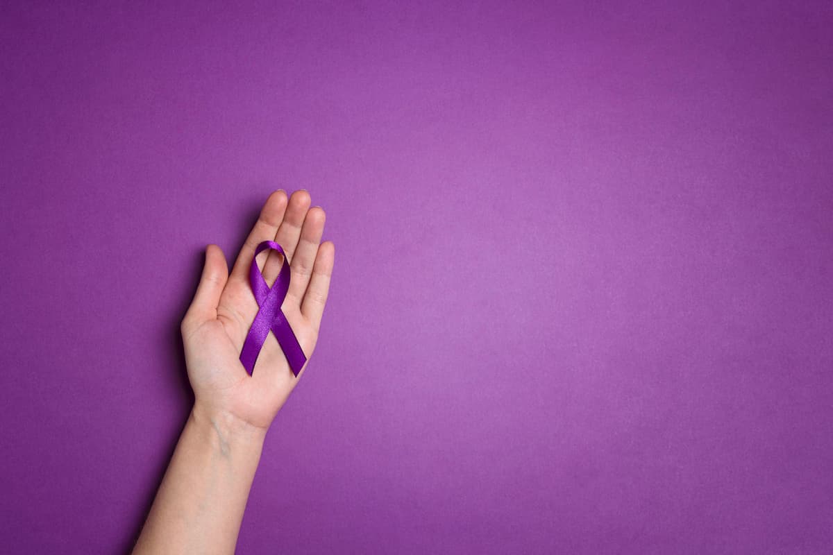 Fundo roxo e mão aberta segurando um laço roxo, símbolo da conscientização sobre a epilepsia e se epilepsia causa impotência no homem