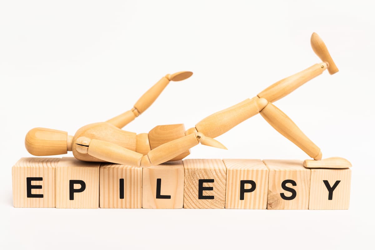 Boneco de madeira caído sobre blocos de madeira em fundo branco que formam a palavra "EPILEPSY" (epilepsia, em inglês) e representam a dúvida se epilepsia causa impotência sexual