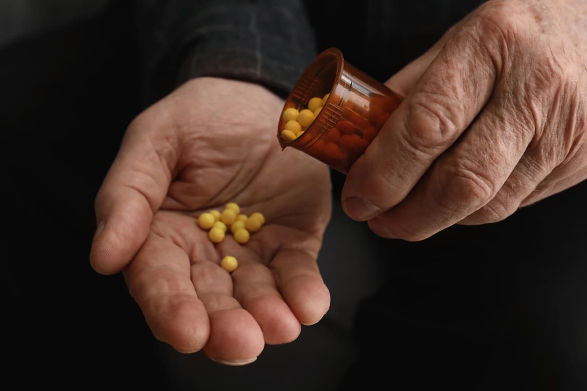 Homem branco e idoso segurando um frasco marrom de comprimidos amarelos, despejando alguns deles na palma da mão, representando se tadalafila aumenta o tamanho peniano