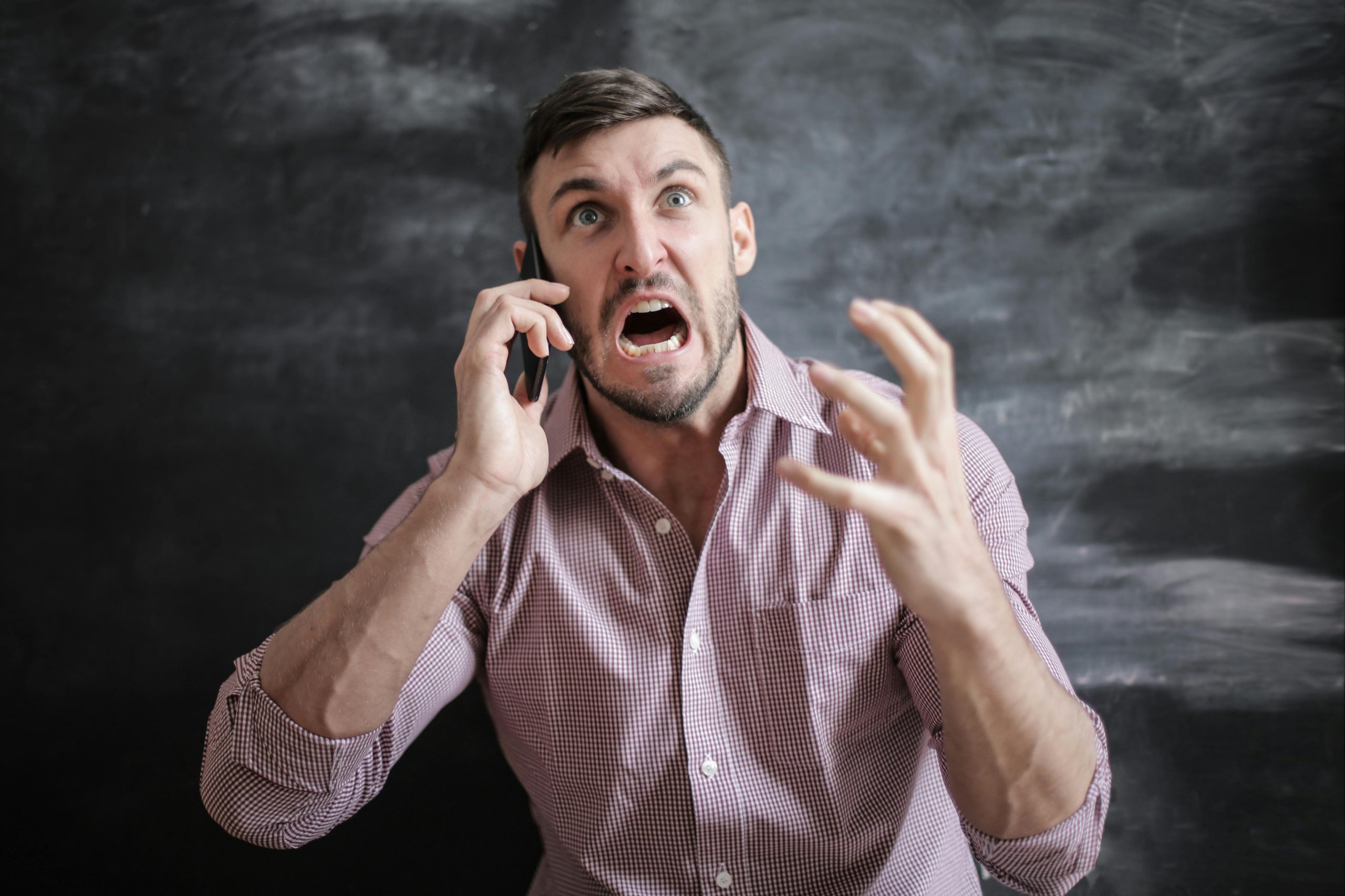 A man on the phone looking frustrated, with one hand raised like a claw, in front of a dark background with white mist