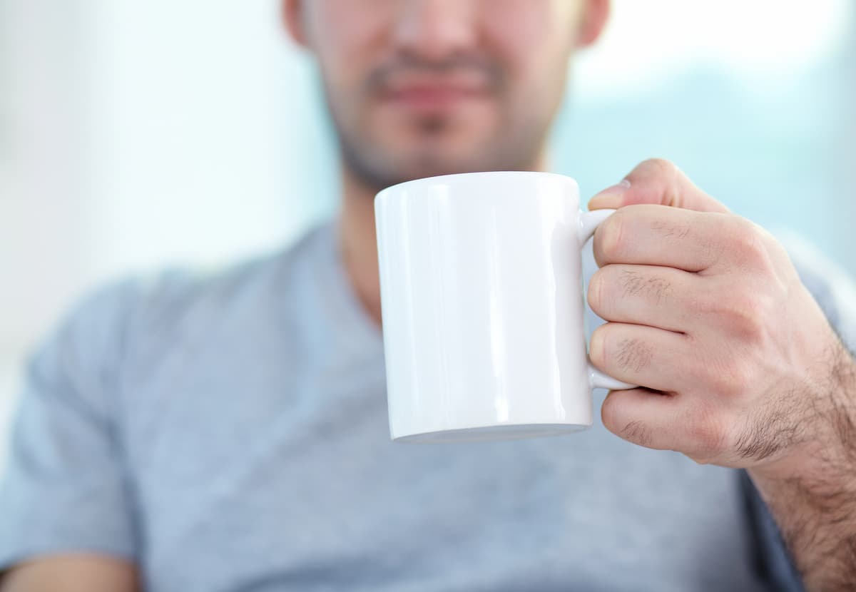 Hombre con camiseta gris sosteniendo una taza blanca con líquido que puede contribuir a la nocturia